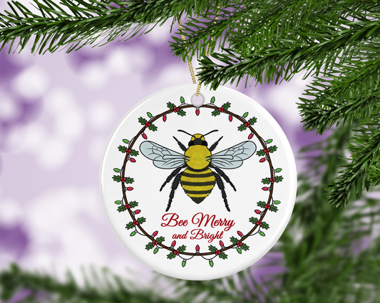 A Christmas Tree decoration with a cute illustration of a bumble bee surrounded by a Christmas wreath with lights, underneath the bee are the positive words of "Bee Merry and Bright".